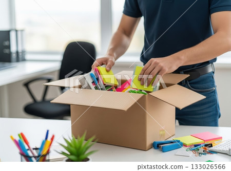 An office worker packs up their belongings and office supplies like sticky notes into a cardboard box as they relocate to a new workplace 133026566