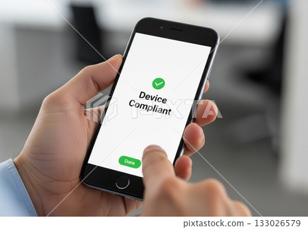 Man touching the screen of his mobile phone that says 'Device Compliant' on the screen indicating successful device compliance 133026579