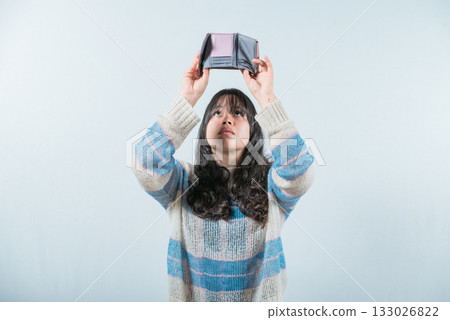 Young woman shaking her empty wallet. Worried girl with no money holding empty wallet, isolated 133026822
