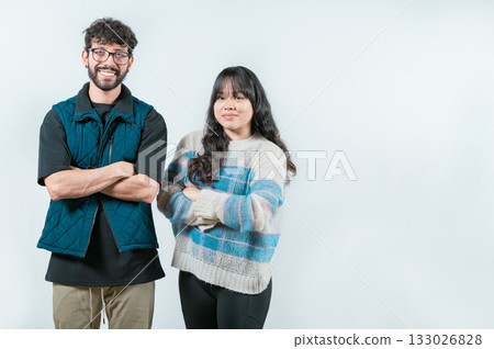 Smiling young couple with crossed arms looking at camera, isolated. Cheerful young multiethnic couple with arms crossed, isolated 133026828