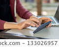 Close up of hand holding and touching on smartphone while sitting with a laptop at concrete table. 133026957
