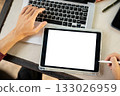 Close up of hand with stylus pointing at white screen tablet on laptop while sitting at table. 133026959