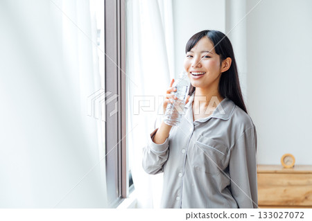 一位年輕女性注重健康的生活方式：早晨喝水的習慣 133027072