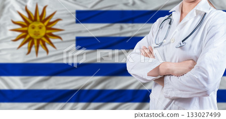 Doctor with crossed arms on Uruguay flag. Uruguay health and care concept. Female doctor on Uruguay flag Doctor with crossed arms on Uruguay flag. Uruguay health and care concept. Female doctor on Uruguay flag 133027499