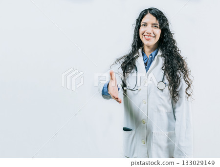 Smiling female doctor gesturing welcome, isolated. Latin female doctor shaking hands at the camera gesturing welcome Smiling female doctor gesturing welcome, isolated. Latin female doctor shaking hands at the camera gesturing welcome 133029149