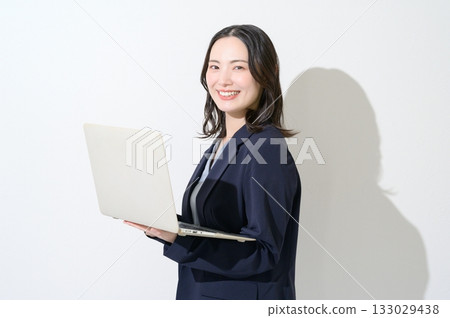 一位日本女性在白色背景下看著鏡頭，她面前放著一台筆記型電腦。 133029438
