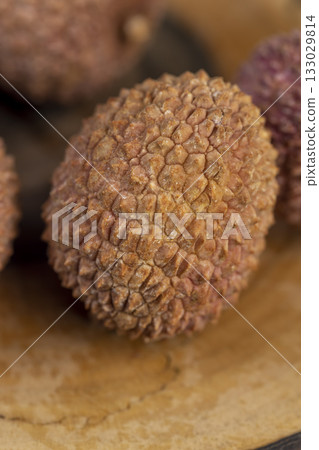 red lychees scattered on a wooden table, ripe red-skinned lychee fruits,rough textured lychee peel closeup red lychees scattered on a wooden table, ripe red-skinned lychee fruits,rough textured lychee peel closeup 133029814