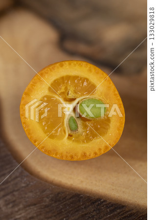 cut ripe kumquat cut in half on a wooden table, a group of scattered and sliced kumquat fruits on a wooden table and board 133029818