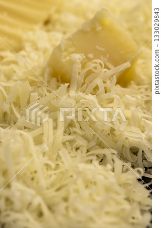 finely grated fresh yellow hard cheese on a metal grater for pizza or pasta, grated cheese with pieces for cooking various foods finely grated fresh yellow hard cheese on a metal grater for pizza or pasta, grated cheese with pieces for cooking various foods 133029843