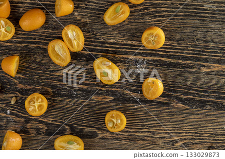 lots of ripe orange kumquat cut in half on a wooden table, a group of scattered kumquat fruits on a wooden table and board lots of ripe orange kumquat cut in half on a wooden table, a group of scattered kumquat fruits on a wooden table and board 133029873