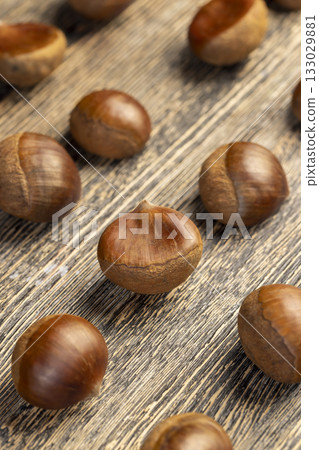 a hard edible chestnut fruit in a brown shell on a wooden table, a group of raw chestnut with a hard shell of brown color 133029881