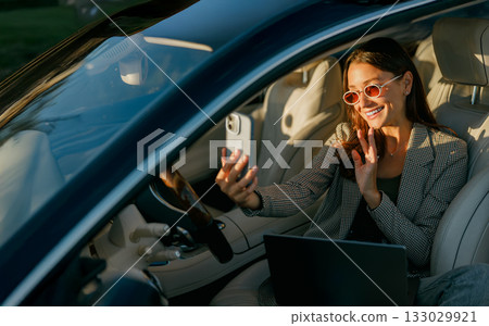 Chic woman taking spontaneous vehicle photo during sunset glow 133029921