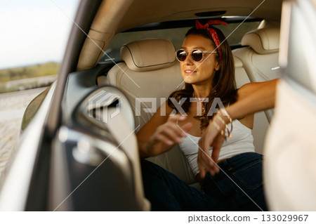 Happy female gesturing from backseat with bright smile and sunglasses 133029967