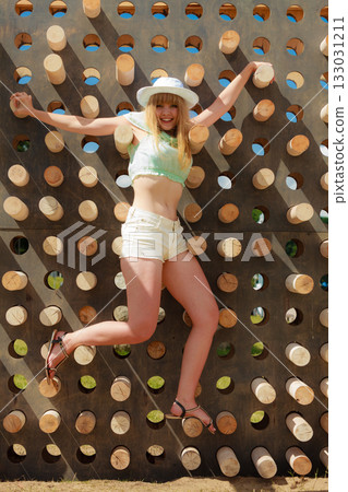 Happy young blonde woman climbing up in adventure park 133031211