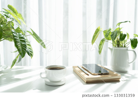 White coffee cup and phone on stack of notebooks with potted plant and sunlight, white minimal work space 133031359