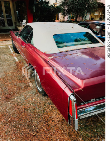 Red vintage convertible car parked on street blanketed with dry pine needles, capturing essence of nostalgia and celebrating classic automotive design in vibrant setting. Retro red convertible  133031418