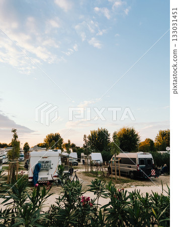 Campers parked in designated spots create tranquil and inviting atmosphere, basking in warm glow of setting sun, perfect for relax and outdoor enjoyment. Camping environment, relaxing outdoor mood 133031451