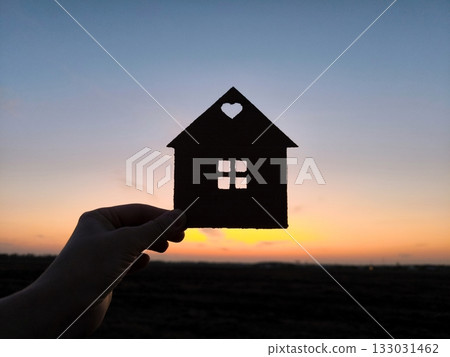 Man holding wooden house model against sunset light for sale or rent, family home and shelter concept, real estate, solar energy and eco accommodation. Man holding wooden house model against sunset light for sale or rent, family home and shelter concept, real estate, solar energy and eco accommodation. 133031462