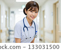 A female nurse with her hair tied up, wearing a stethoscope around her neck and smiling gently in a hospital corridor 133031500