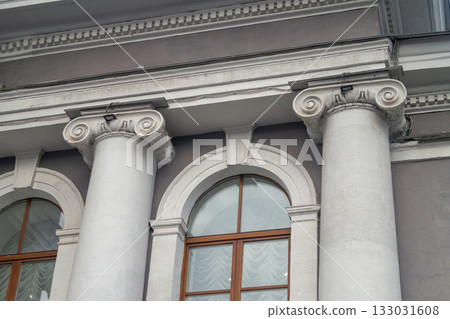 Facade fragment of an old classicism style building with Ionic columns and an arched window. Architectural background symbolizing justice, government, education, or culture and finance. 133031608