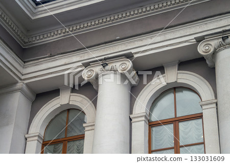 Facade fragment of an old classicism style building with Ionic columns and an arched window. Architectural background symbolizing justice, government, education, or culture and finance. 133031609