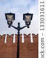 Vintage black forged street lamp against an old red brick fortress wall with battlements. Urban background for the concept of history, security, and city street illumination. 133031611