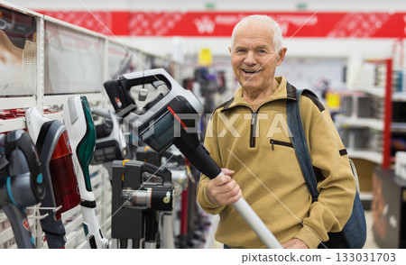 elderly man choosing Upright Vacuum hoover in showroom of electrical appliance store 133031703