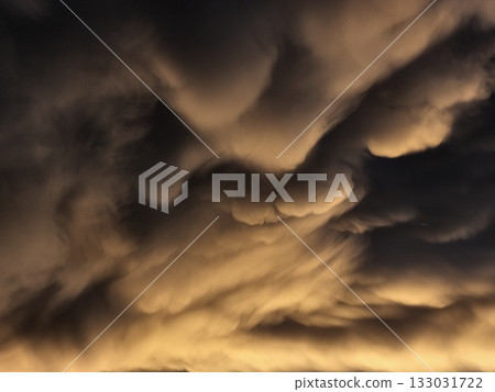 Storm clouds on sunset. Light in the dark and dramatic storm clouds. Background of storm clouds before a thunderstorm. Mammatus clouds Storm clouds on sunset. Light in the dark and dramatic storm clouds. Background of storm clouds before a thunderstorm. Mammatus clouds 133031722