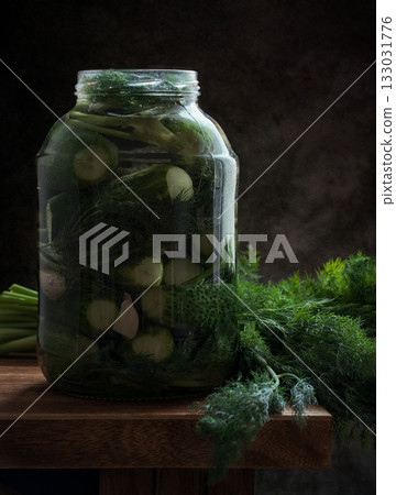 Rustic arrangement of pickled cucumbers in a jar, garlic, and dill on a dark background. Ideal for culinary, organic, or homemade food themes. 133031776