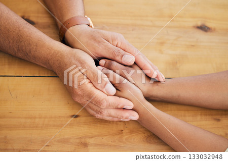 Top view of couple holding hands on table for love, care and empathy of mental health, trust and counseling. Closeup people, helping hand and support on wooden surface for gratitude, kindness or hope 133032948