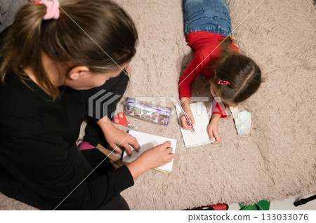 Mother and daughter enjoy creative time together at home drawing on the carpet, fostering imagination and bonding through art. 133033076