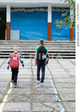 Two young boys with backpacks are walking towards a building, likely heading to school on a paved path with colored lines marking the way. Two young boys with backpacks are walking towards a building, likely heading to school on a paved path with colored lines marking the way. 133033093