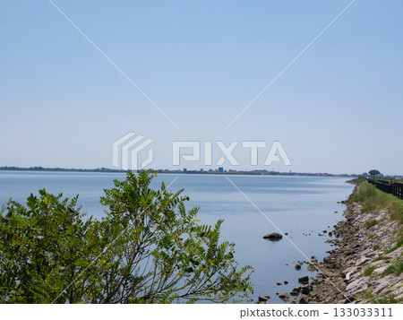 Grado, Italy - July 30th 2024: Dam towards the touristic village of Grado behind the lagoons and islands Grado, Italy - July 30th 2024: Dam towards the touristic village of Grado behind the lagoons and islands 133033311