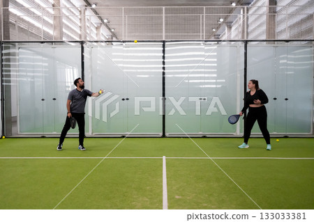 Man and woman playing padel tennis inside a modern indoor court Man and woman playing padel tennis inside a modern indoor court 133033381