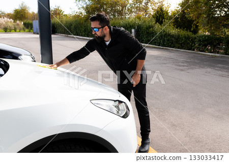 Young caucasian male cleans car hood at outdoor car wash 133033417