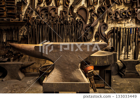 Workshop, metal tools and anvil in forge with wall background for industry, manufacturing or development. Retro factory, workspace or industrial for steel, iron or product with vintage craftsmanship Workshop, metal tools and anvil in forge with wall background for industry, manufacturing or development. Retro factory, workspace or industrial for steel, iron or product with vintage craftsmanship 133033449