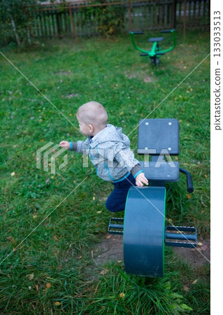 Child explores outdoor fitness equipment, engaging in playful activities within a grassy park setting on a cloudy day, promoting active lifestyles. 133033513