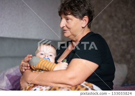 Grandmother and baby sharing a tender moment, expressing love and care in a cozy, intimate setting, creating a heartwarming family image. Grandmother and baby sharing a tender moment, expressing love and care in a cozy, intimate setting, creating a heartwarming family image. 133033824