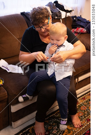 Grandmother carefully clipping a young boy's nails on a couch, showing love and care in a cozy home setting. Cherished generational moment. 133033848