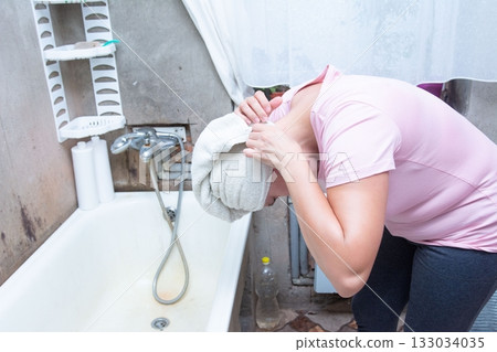 Woman in pink bends over bathtub, wearing a towel wrapped around her head in a bathroom setting Woman in pink bends over bathtub, wearing a towel wrapped around her head in a bathroom setting 133034035