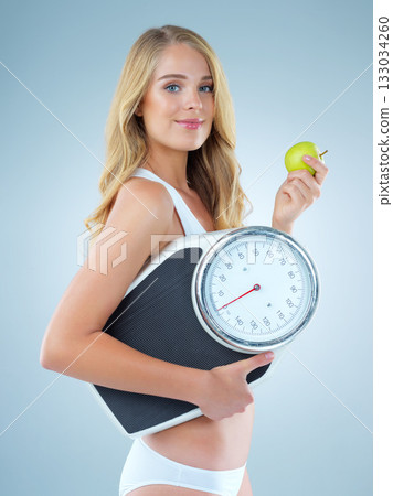 Woman in portrait, apple with scale and lose weight, smile with healthy food isolated on studio background. Happy female model, health and diet with organic fruit with nutrition and weightloss Woman in portrait, apple with scale and lose weight, smile with healthy food isolated on studio background. Happy female model, health and diet with organic fruit with nutrition and weightloss 133034260