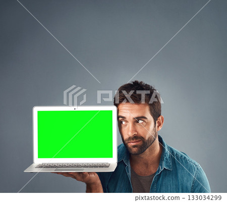Man, laptop and thinking on mockup green screen for advertising or marketing against a grey studio background. Thoughtful male person showing computer display, mock up or copy space for advertisement 133034299