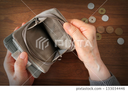 A woman's hand opening an empty wallet and coins on a table 133034446