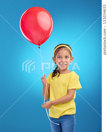 Happy girl, studio and red balloon of a an excited kid with a smile ready for a birthday party. Celebration, happiness and young child holding balloons in the air with isolated blue background Happy girl, studio and red balloon of a an excited kid with a smile ready for a birthday party. Celebration, happiness and young child holding balloons in the air with isolated blue background 133034655