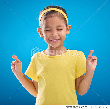 Child, hand and fingers crossed in studio for hope, wish or good luck against a blue background. Girl, eyes closed and emoji hands, praying and wishing, happy and smile while posing on isolated space Child, hand and fingers crossed in studio for hope, wish or good luck against a blue background. Girl, eyes closed and emoji hands, praying and wishing, happy and smile while posing on isolated space 133034667