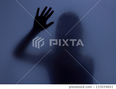 Shadow, glass and hand with a woman in studio on a blue background for mystery or sensual secrecy. Creative, silhouette and window with a female posing for beauty, art deco or feminine desire Shadow, glass and hand with a woman in studio on a blue background for mystery or sensual secrecy. Creative, silhouette and window with a female posing for beauty, art deco or feminine desire 133034681