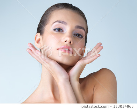 Makeup, woman and hands on face in studio for skincare, wellness or cosmetic on blue background. Portrait, beauty and girl model with dermatology, satisfaction or luxury skin routine while isolated Makeup, woman and hands on face in studio for skincare, wellness or cosmetic on blue background. Portrait, beauty and girl model with dermatology, satisfaction or luxury skin routine while isolated 133034963