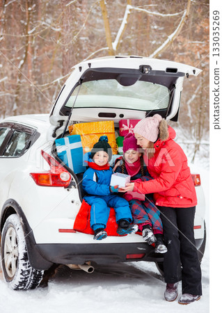 Smiling mom with her kids surrounded by holiday gift boxes in back of snowy car, enjoying magical winter forest day. Merry Christmas 133035269