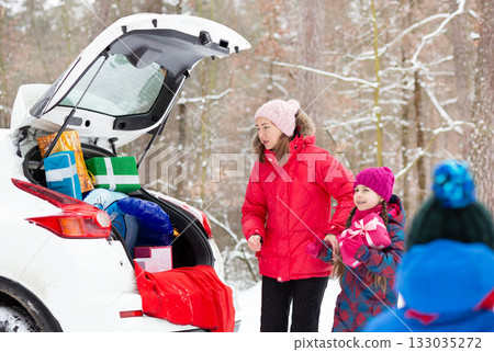 Smiling mom with her kids surrounded by holiday gift boxes in back of snowy car, enjoying magical winter forest day. Merry Christmas Smiling mom with her kids surrounded by holiday gift boxes in back of snowy car, enjoying magical winter forest day. Merry Christmas 133035272