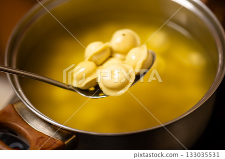 Spoon with Boiled Dumplings Over Pot of Broth 133035531